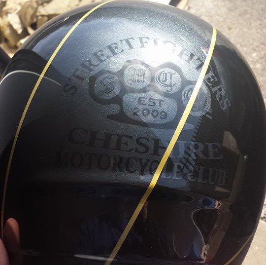 Airbrushed Painting of a Grey Black and Gold Helmet with Street fighters Cheshire Logo design